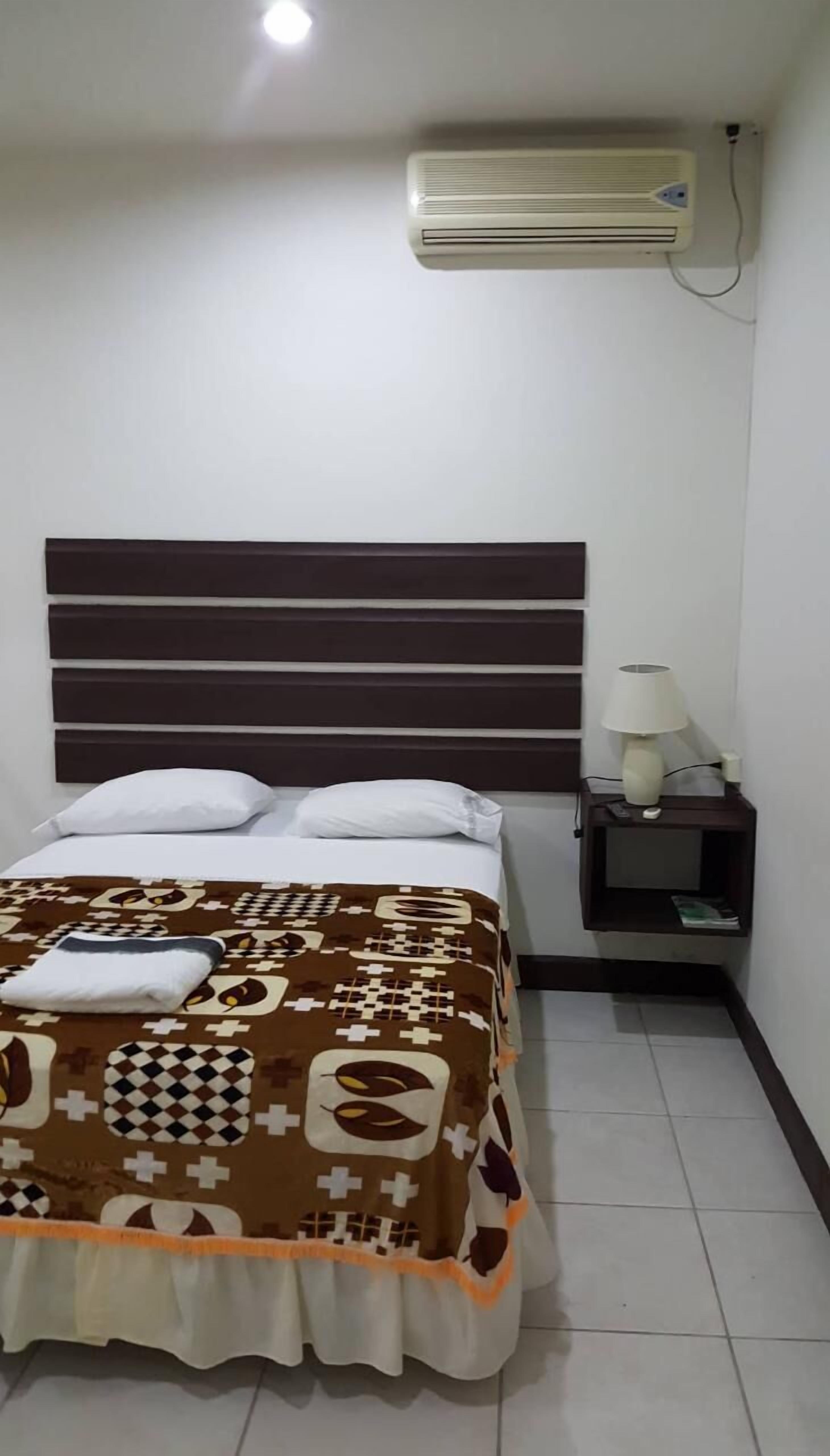 A bedroom with a bed, a bedside table with a lamp, and an air conditioning unit on the wall.