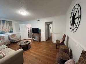 A living room with a television, wicker furniture, and a sailboat painting.