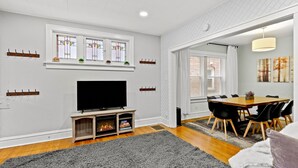 Una sala de estar con chimenea, un televisor de pantalla plana, un comedor con mesa y sillas de madera, y un ventanal con vidrieras.
