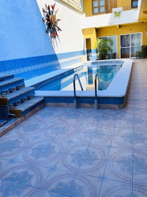 A swimming pool with steps leading up to it, surrounded by blue-tiled flooring and a yellow building in the background. - cosy place at Turtles Condo on sun house  (Lomas del Calvario)