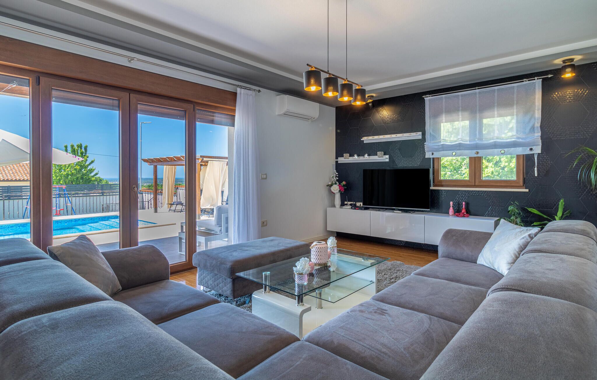 Una sala de estar moderna con una mesa de centro de vidrio, sofás grises, un televisor de pantalla plana y vistas a la piscina.