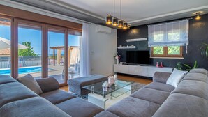 A modern living room with a glass coffee table, grey sofas, a flat-screen TV, and a pool view. - Pet friendly home in Vodnjan (Vodnjan)