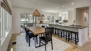 A modern kitchen with a central island, bar stools, and a dining area with a wooden table and chairs.