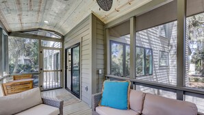 A covered porch with wicker furniture, a sliding glass door, and a view of the surrounding area.