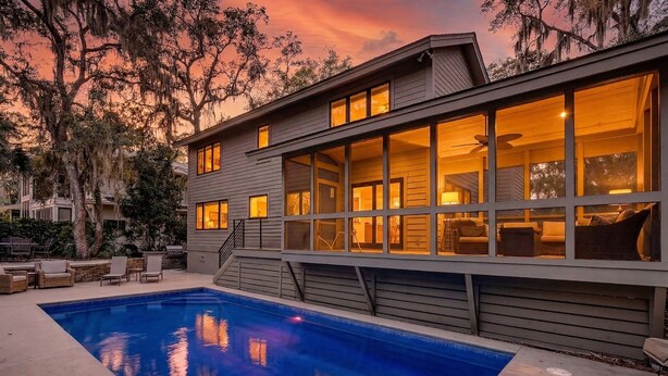 A modern house with a swimming pool, large windows, and outdoor furniture.