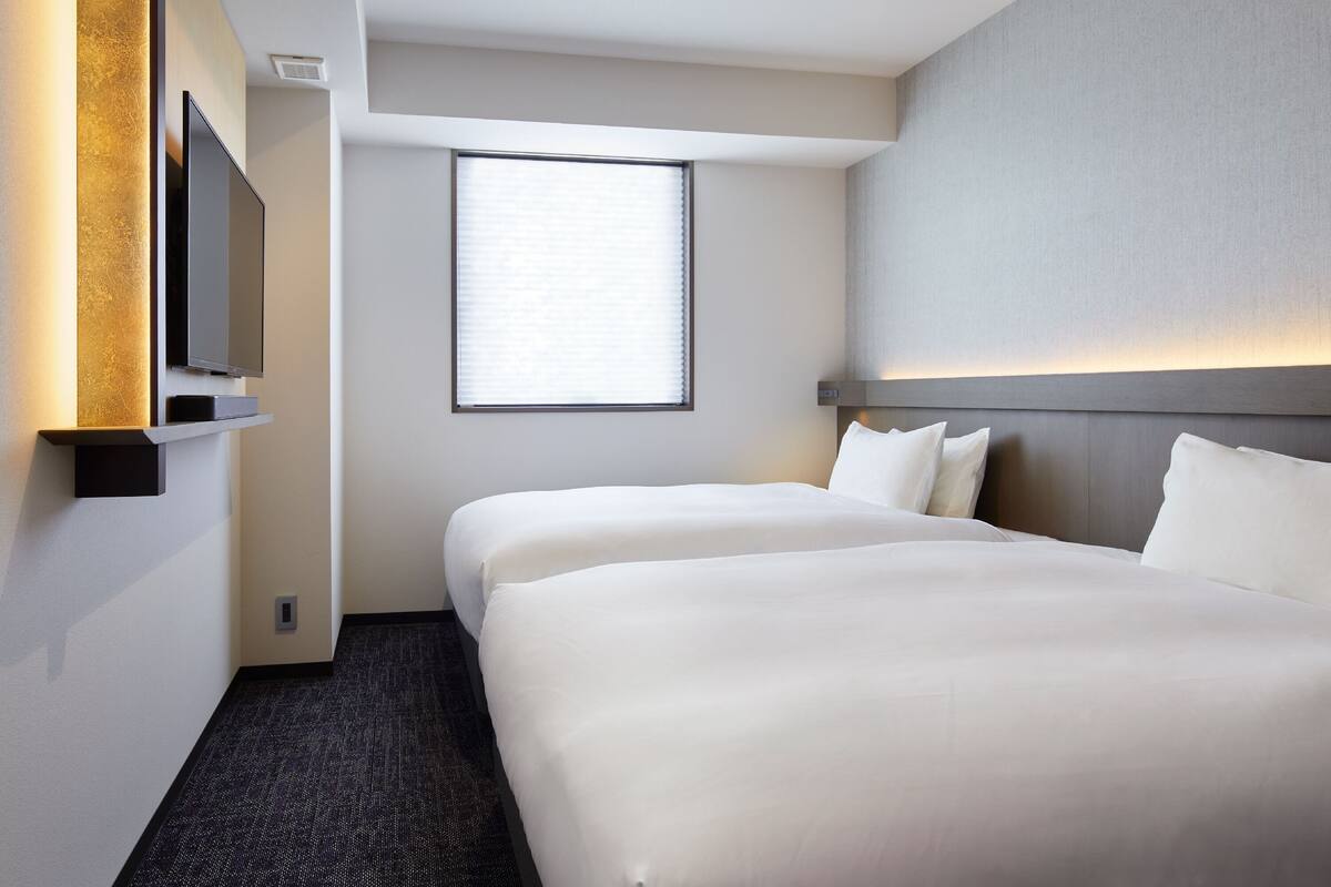 A hotel room with two beds, a television, and a window with blinds.