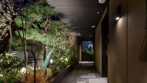 A corridor with a concrete floor, a low wall on one side, and a variety of plants and trees. - Agora Tokyo Ginza (Tokyo)