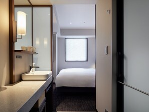 Habitación de hotel con cama, baño con lavamanos y ventana con persianas.