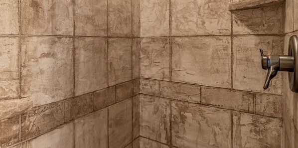 A corner of a room with tiled walls and a corner shower fixture.
