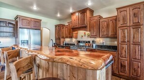 A kitchen with wooden cabinets, a central island with a bench, and a stainless steel refrigerator.