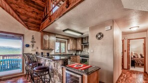 A kitchen with a stone island, wooden bar stools, and a view of the mountains.