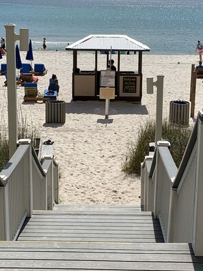 Une promenade en bois menant à une plage, avec un espace de repos abrité et des poubelles.