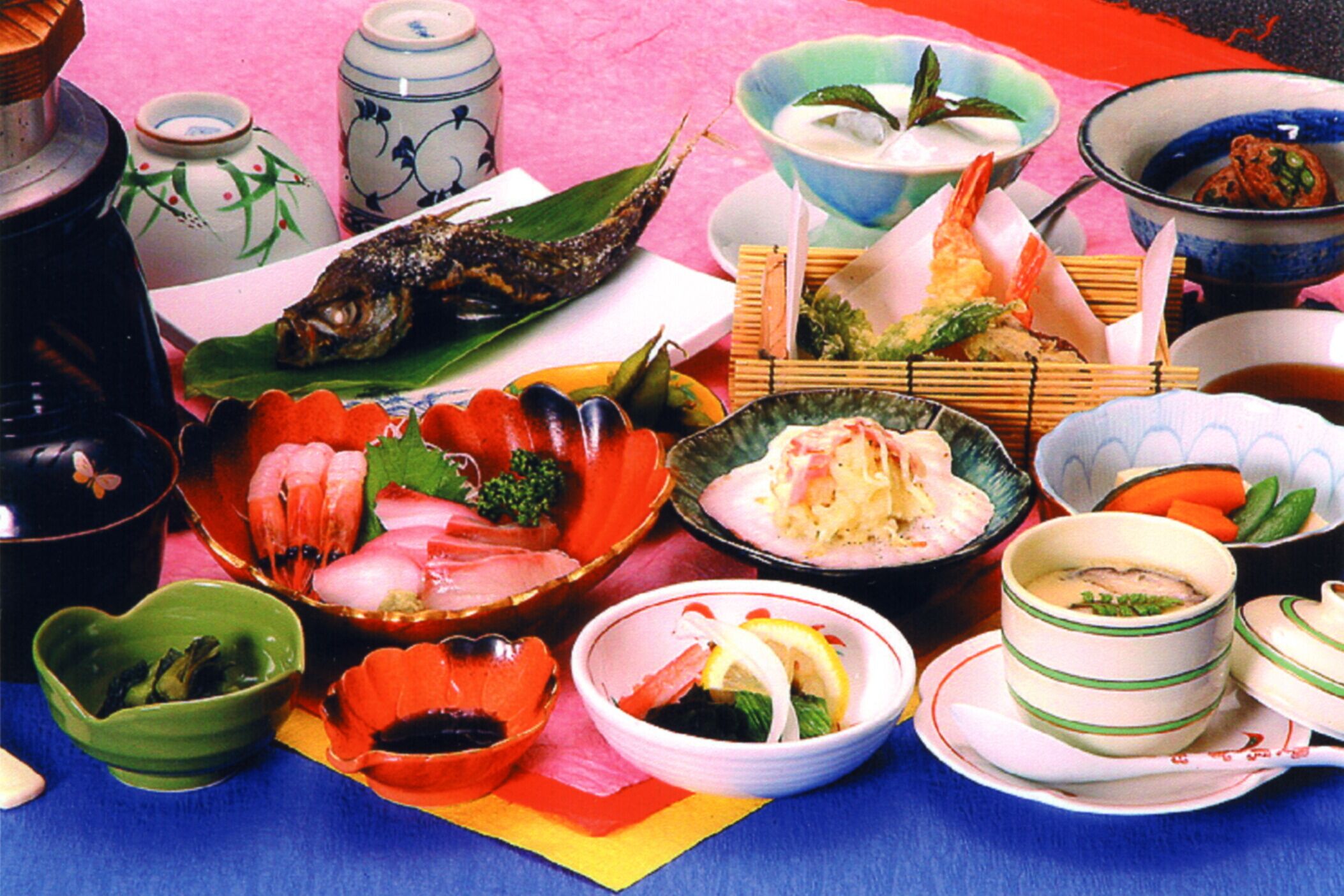 A table with various dishes and bowls, including seafood and vegetables, arranged on a colorful tablecloth.