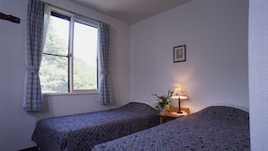 Ein Zimmer mit zwei Einzelbetten, einem Fenster mit Vorhängen, einem Nachttisch mit Lampe und einem gerahmten Bild an der Wand.