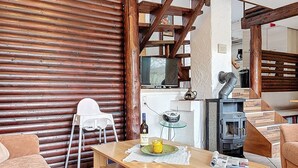 A cozy living room with a wooden table, a sofa, a white chair, a fireplace, and a television. - Am Sternberg 38 by Interhome (Frankenau)