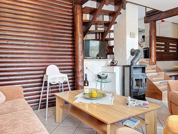 Ein gemütliches Wohnzimmer mit einem Holztisch, einer Couch, einem weißen Sessel, einem Kamin und einem Fernseher.