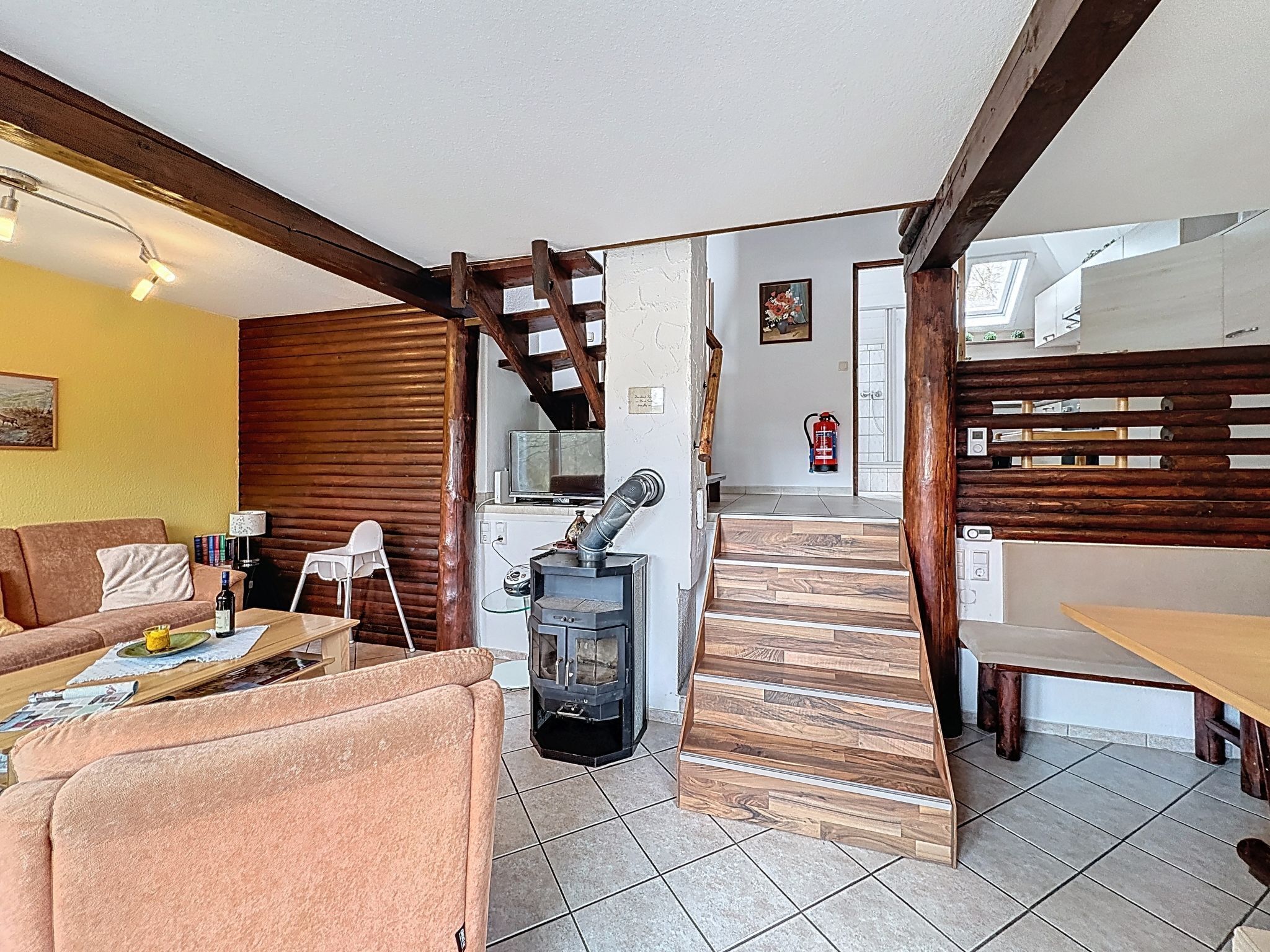 Un salon comprenant un canapé, une table, une cheminée, un escalier et un coin cuisine.