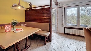 A dining area with a wooden table, benches, a hanging light fixture, and a window with a view of trees. - Am Sternberg 38 by Interhome (Frankenau)