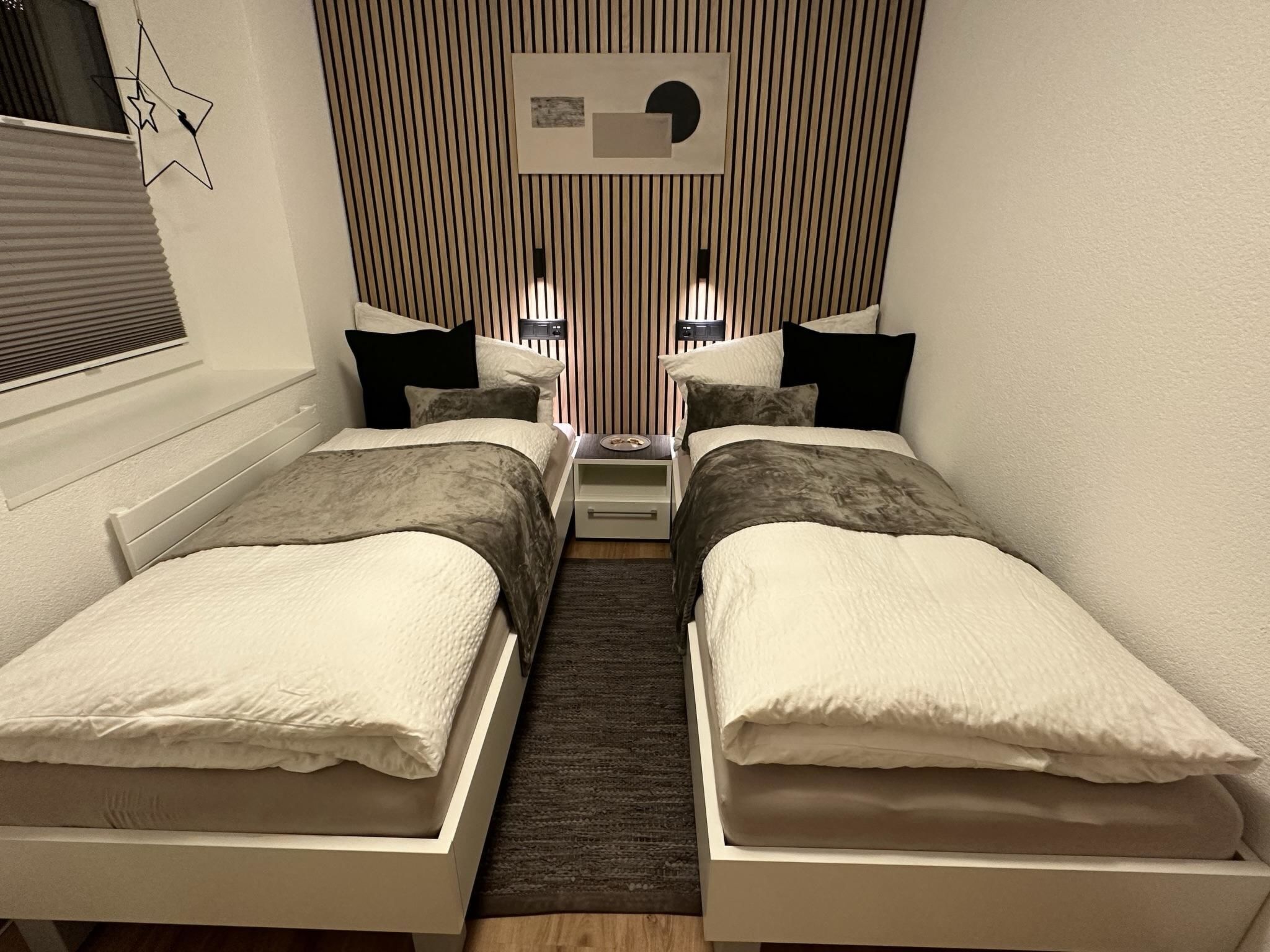 Un dormitorio pequeño y moderno con dos camas individuales, una mesita de noche, un estante en la pared y un adorno con forma de estrella.