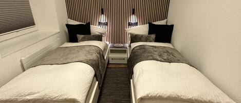 Un dormitorio pequeño y moderno con dos camas individuales, una mesita de noche, un estante en la pared y un adorno con forma de estrella.