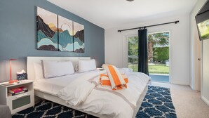 A modern bedroom with a large bed, a nightstand, a ceiling fan, and a view of the outdoors through a sliding door.
