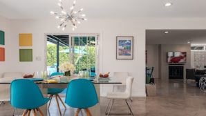 A modern kitchen with a dining area, featuring a white countertop, teal chairs, and a unique chandelier.