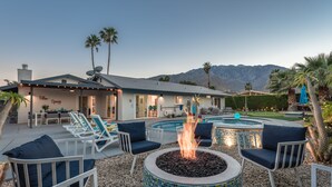 A pool area with lounge chairs and a fire pit, surrounded by a house with a mountain view.