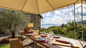 Mesa para comer al aire libre con platos, cubiertos y una botella de vino, con vistas a un paisaje pintoresco.