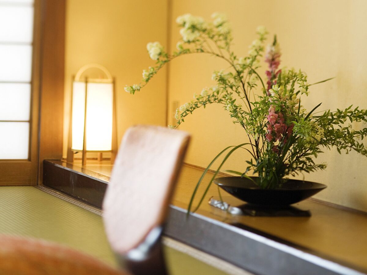 Ein traditioneller japanischer Raum mit Tatami-Böden, einem niedrigen Holztisch und einer schwarzen Schale mit Blumenarrangement.