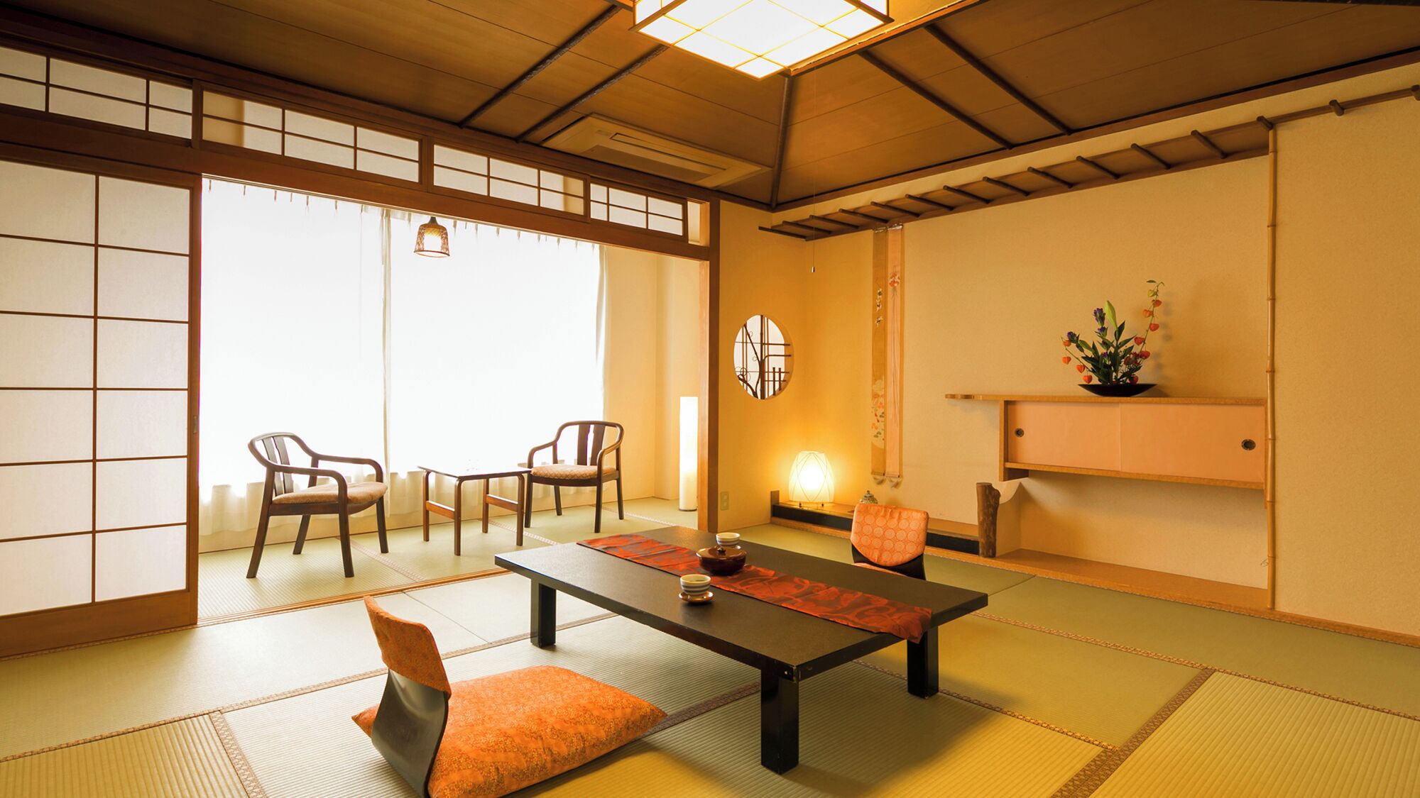 A traditional Japanese room with tatami flooring, a low table, chairs, and a sliding door.