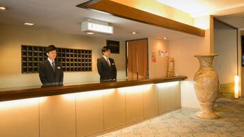 A reception desk with two staff members, a large vase, and a patterned floor.