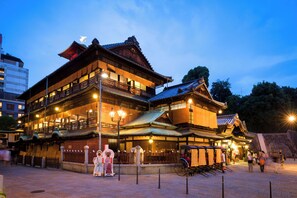 A traditional Japanese building with multiple floors and a tiled roof, featuring a prominent entrance and a small shrine area in front. - Dogo Grand Hotel (Matsuyama)