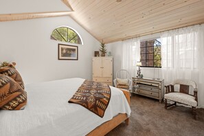 A bedroom with a bed, a dresser, a chair, and a window with curtains. - Junipine Lakefront Condo - Boulder Bay | Pool + Tennis | Walk to Lake (Big Bear Lake)