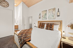 A bedroom with a bed, a nightstand, a wall clock, and a window. - Junipine Lakefront Condo - Boulder Bay | Pool + Tennis | Walk to Lake (Big Bear Lake)