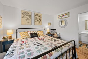 A bedroom with a bed, two nightstands, a chair, a mirror, and wall decorations including botanical illustrations and a framed picture of birds.