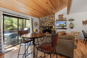 A cozy living room with a stone fireplace, wooden ceiling, and a large window overlooking a deck.