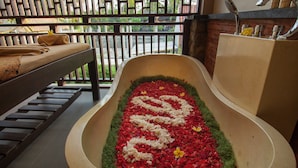 A bathtub filled with red and white flowers, a wooden bench, and a sink with a faucet. - The Mudru Resort by GenuineHost (Sukawati)