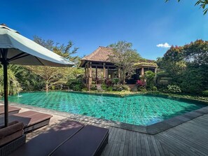 A clear blue pool with lounge chairs and a wooden deck. - The Mudru Resort by GenuineHost (Sukawati)