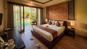 A hotel room with a large bed, a desk with a telephone, a TV, and a view of an outdoor pool area. - The Mudru Resort by GenuineHost (Sukawati)