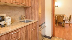 A compact kitchen with wooden cabinets, a granite countertop, a coffee maker, and a built-in dishwasher. - Dent Favre A 5 by Interhome (Ovronnaz)