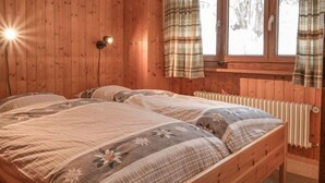 A wooden room with a bed, a window with curtains, and a wall-mounted light fixture. - Dent Favre A 5 by Interhome (Ovronnaz)