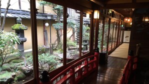 Een traditionele Japanse gang met houten vloeren en rode leuningen, die uitkomt op een tuin met rotsen, planten en een stenen lantaarn.