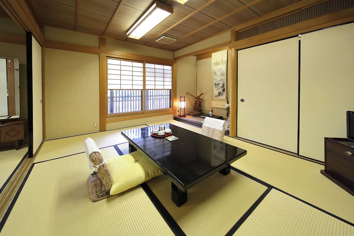 Ein Raum mit Tatami-Matten, einem schwarzen Tisch, Kissen, einem Windrad und Schiebetüren.