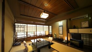 Een traditionele Japanse kamer met tatami vloerbedekking, een lage tafel, een bank, een televisie en een groot raam met shoji schermen.