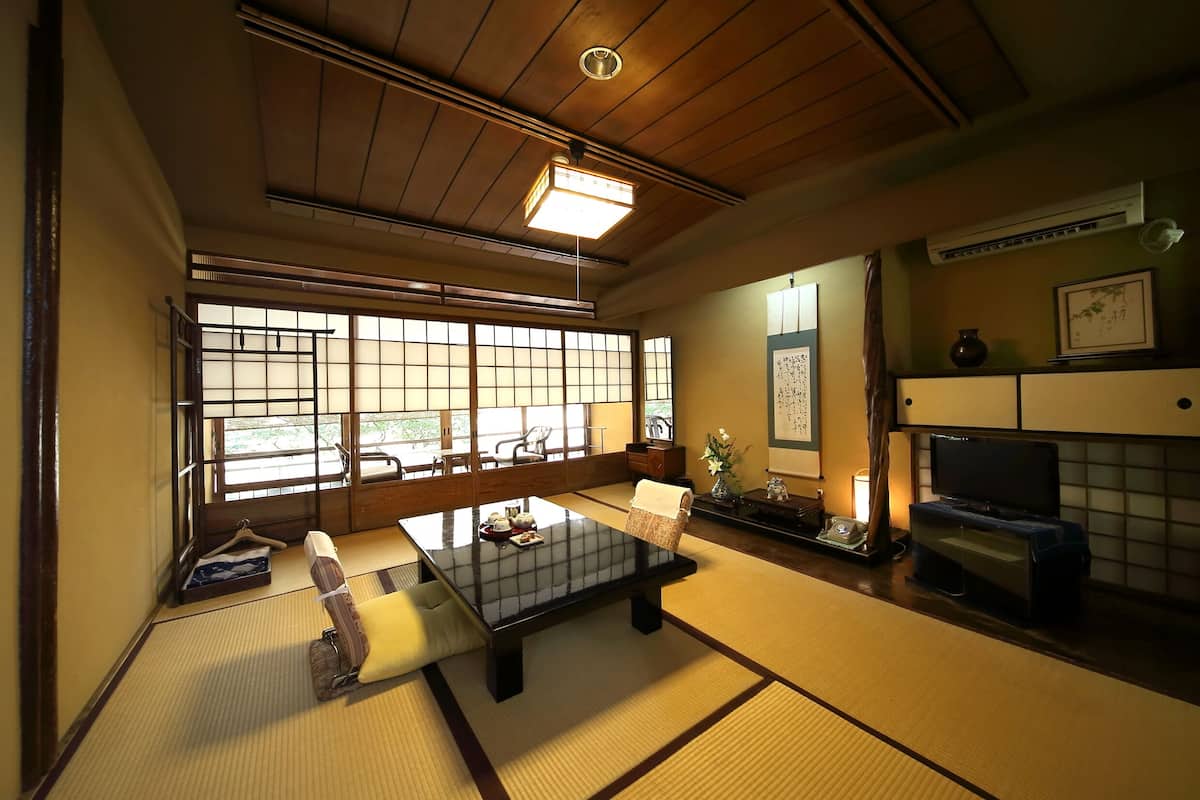 Een traditionele Japanse kamer met tatami vloerbedekking, een lage tafel, een bank, een televisie en een groot raam met shoji schermen.