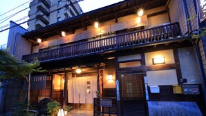 Een traditionele Japanse herberg met een houten balkon, een naambord en een goed verlichte ingang.