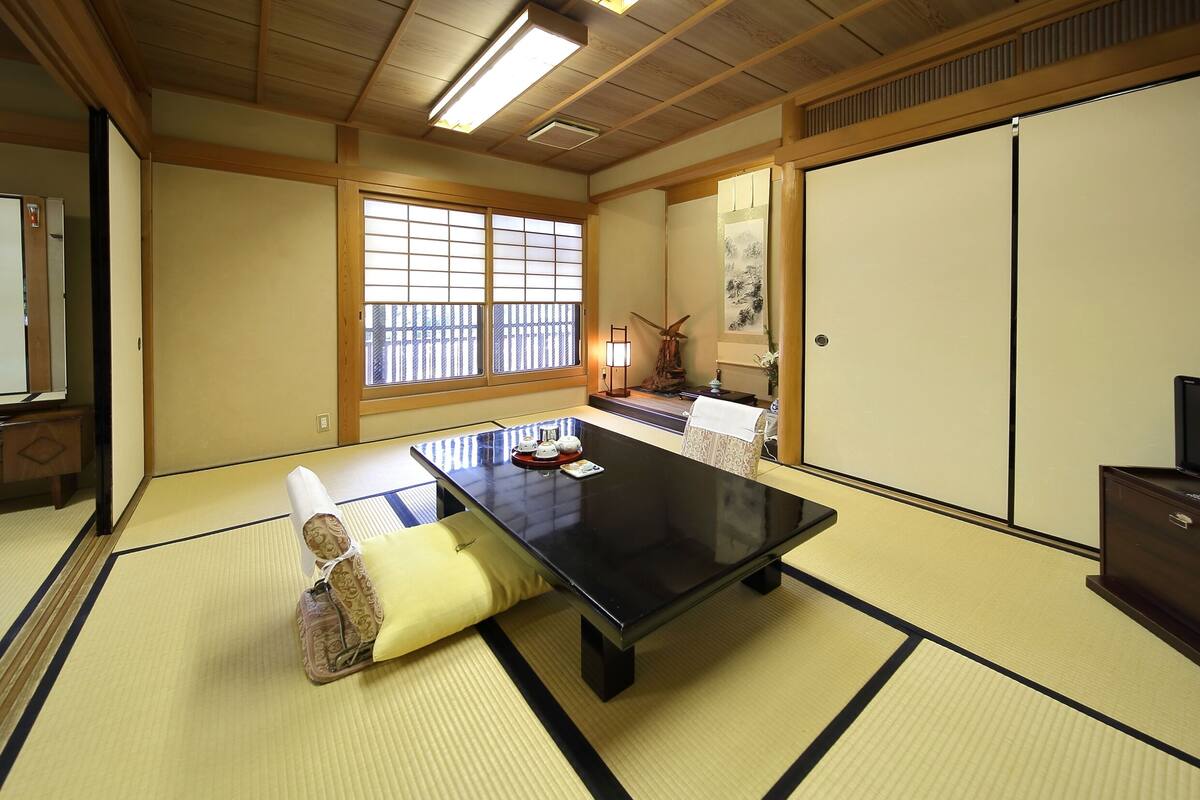 Een kamer met tatami matten, een zwart tafel, kussens, een windmolen en schuifdeuren.