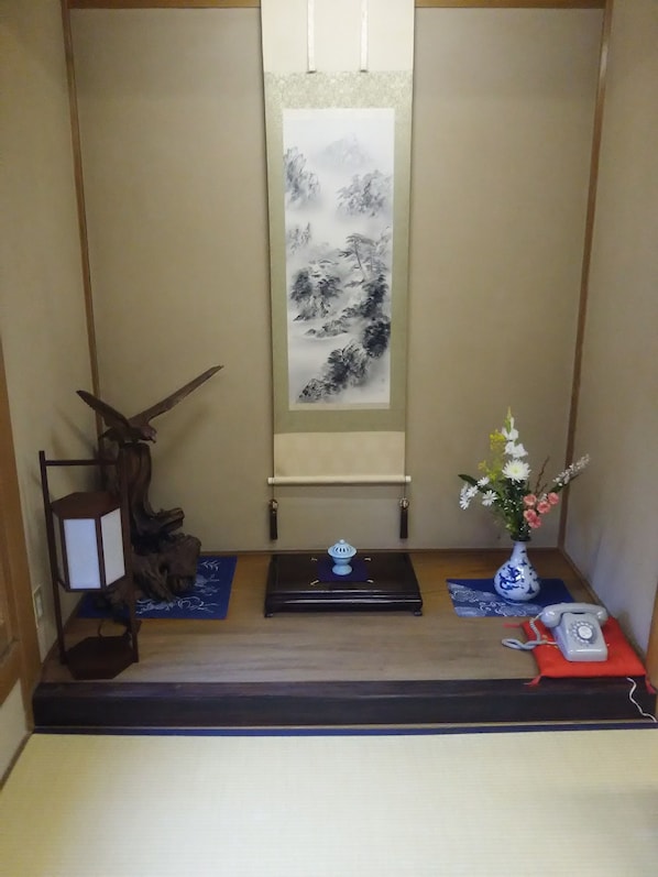 A traditional Japanese room with tatami flooring, a shoji screen, a calligraphy scroll, a wooden sculpture, a vase with flowers, and a red telephone. - Yadoya Kikokuso (Kyoto)