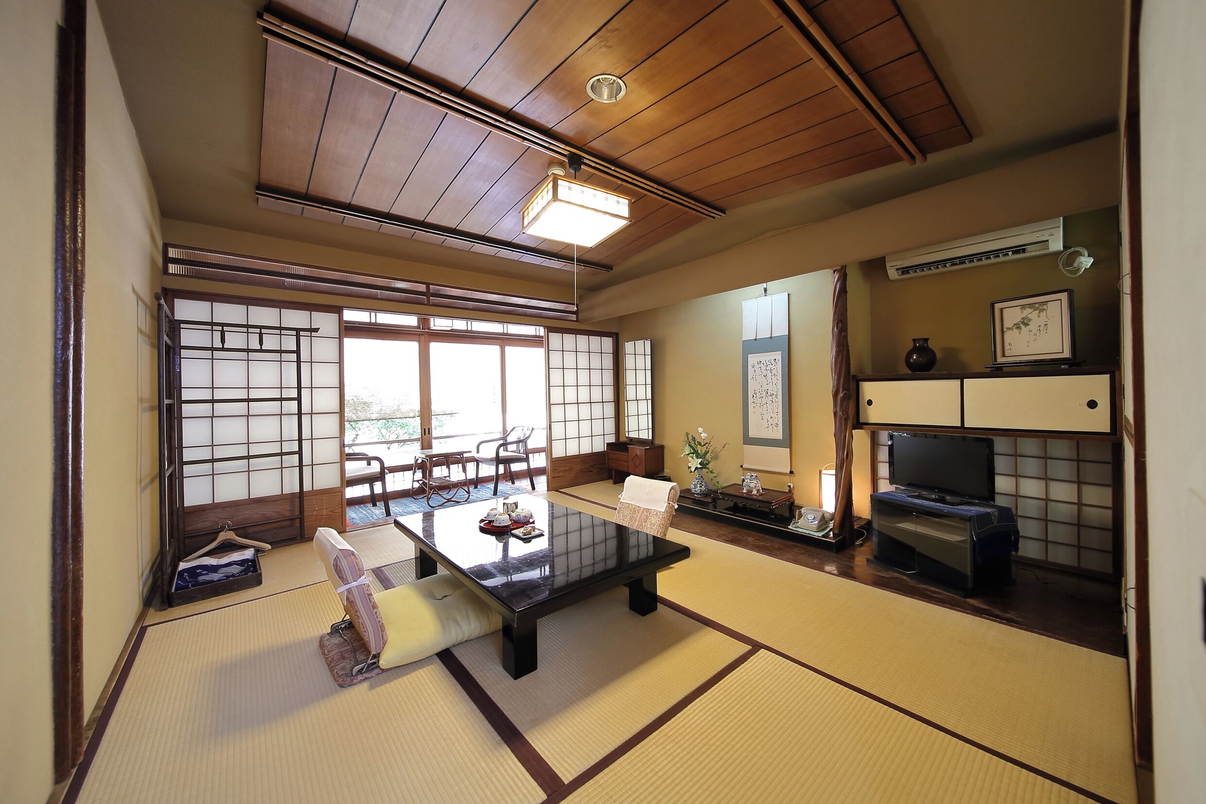 Une pièce de style japonais traditionnel, avec un sol recouvert de tatamis, une table basse, un téléviseur et une porte coulissante donnant sur un coin repas.