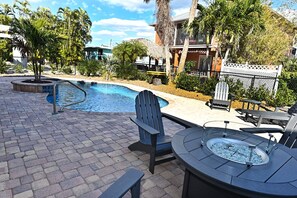 A pool area with a hot tub, lounge chairs, and a thatched-roof structure.